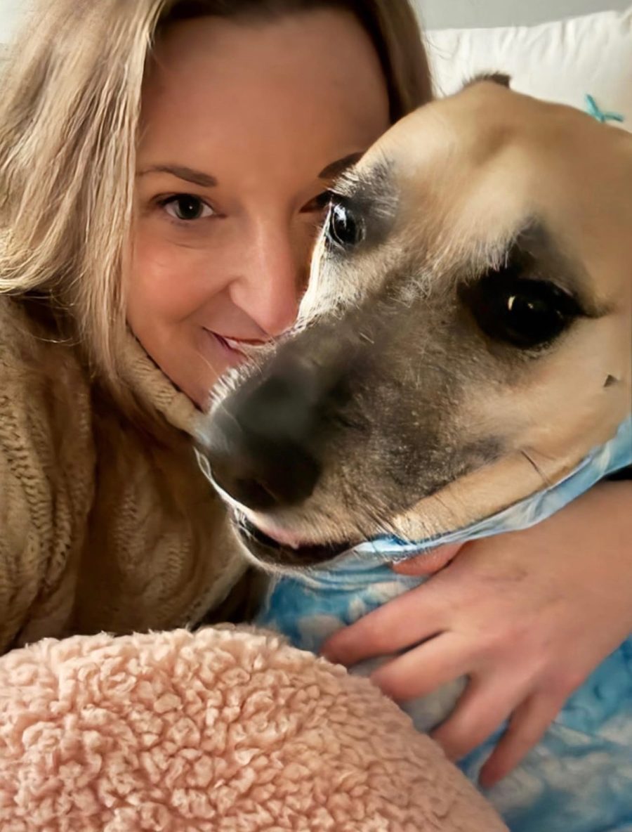 Elyse smiling and hugging her dog, Emma, who is wrapped in a blue blanket